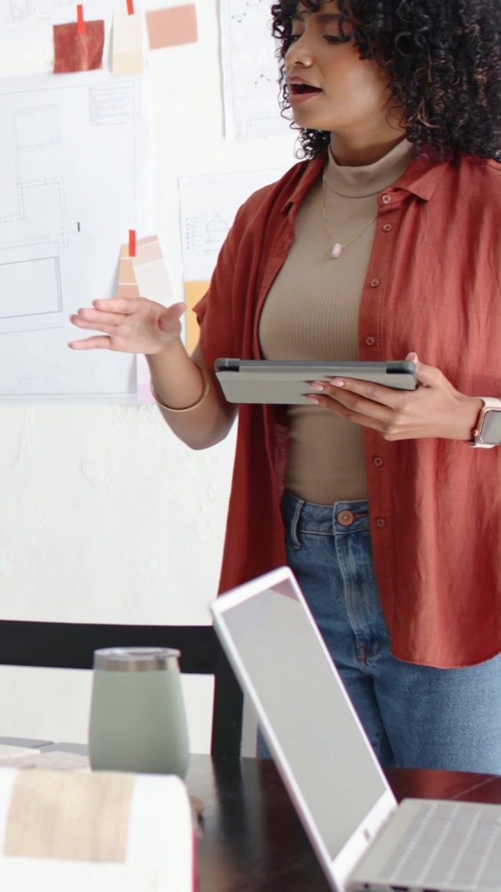 Vertical video: Holding tablet woman in rust top checking plans in studio as peer taking yellow pen