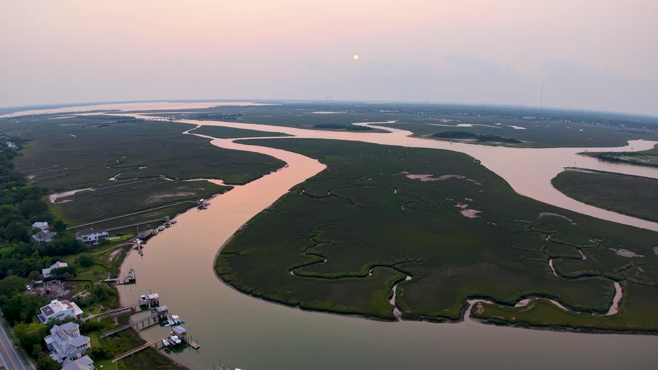 Aerial drone footage glides over a winding river snaking through lush wetlands during sunset, capturing shimmering water and surrounding greenery
