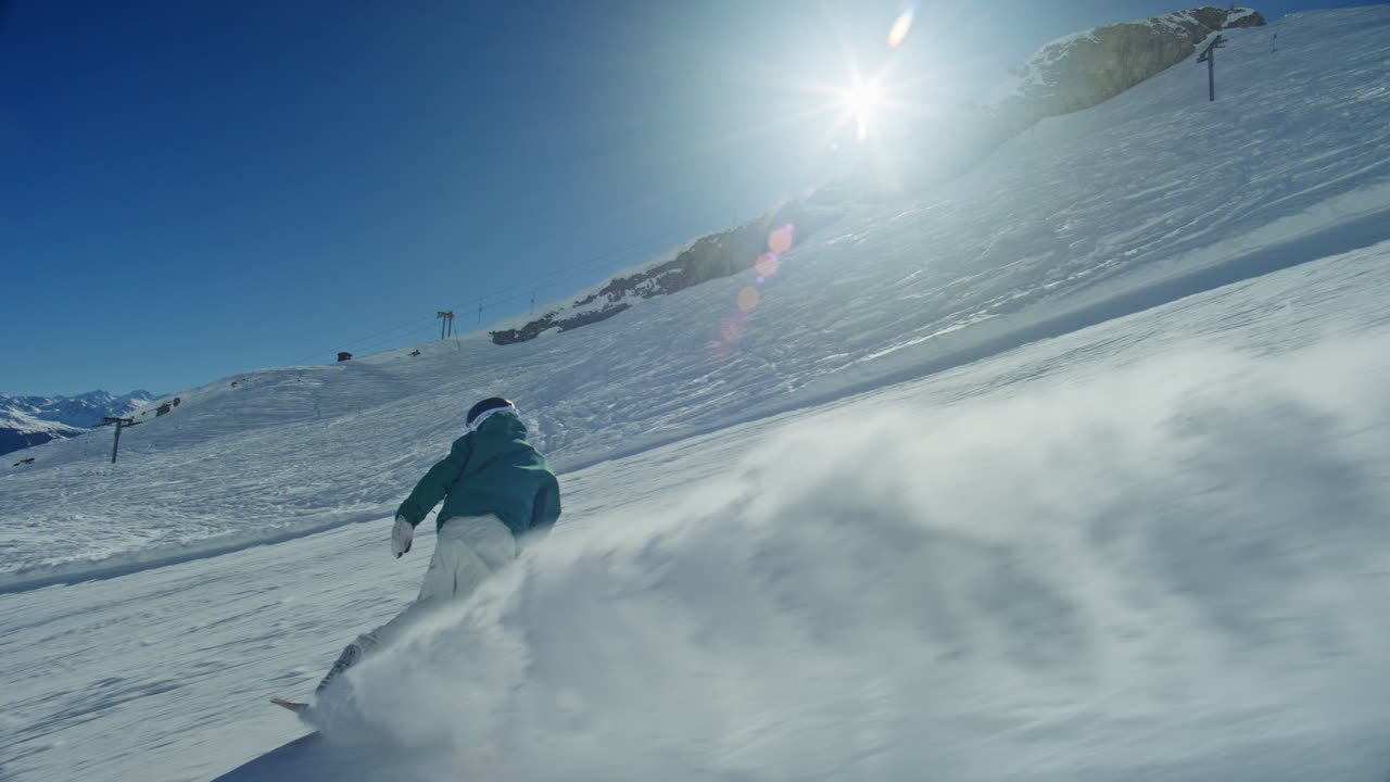 Ripresa con telecamera a seguire di uno snowboarder che scia su una pista battuta ad Anzère in una giornata di cielo sereno e soleggiato, eseguendo curve potenti e sollevando spruzzi di neve. Luce alpina nitida, azione dinamica di sport invernali, resa cinematografica.