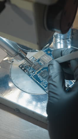 vista de cerca de la mano de un técnico usando un microscopio para examinar y reparar una placa de circuito, el espacio de trabajo está lleno de herramientas de precisión
