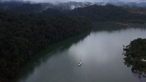 Luftaufnahme-Aus-Der-Luft-Eines-Segelboots,-Das-Im-Nebligen-Tropenwald-Den-Fluss-Hinauffährt