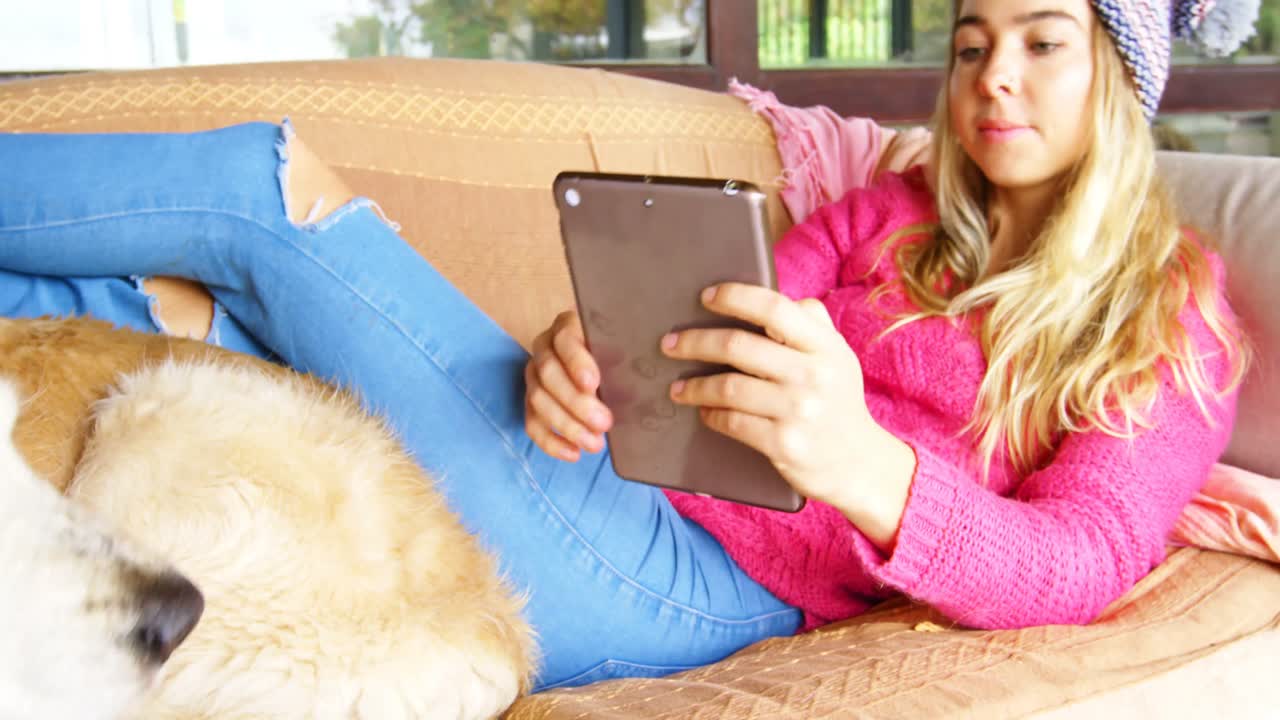 mujer acariciando a su perro mientras usa una tableta digital en el sofá 4k