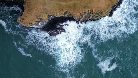 A-bird's-eye-view-of-strong-waves-crashing-against-a-cliff-at-Skeidararsandur,-Iceland