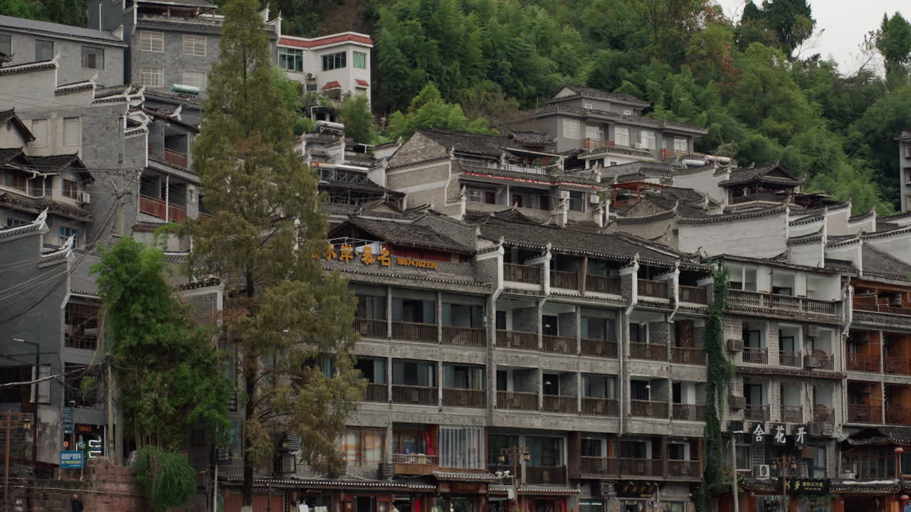 Blocos de apartamentos na encosta acima do rio, com fachadas de concreto e varandas empilhadas. Uma densa grade residencial com becos estreitos, árvores altas e vegetação no topo da colina, com sinais de decadência e renovação, e a comunidade.