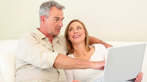 una pareja madura usando una computadora portátil juntos en el sofá.