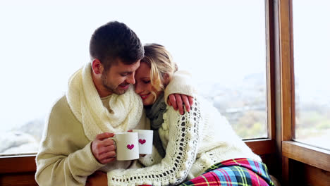 cute couple cuddling together under a blanket in their ski lodge