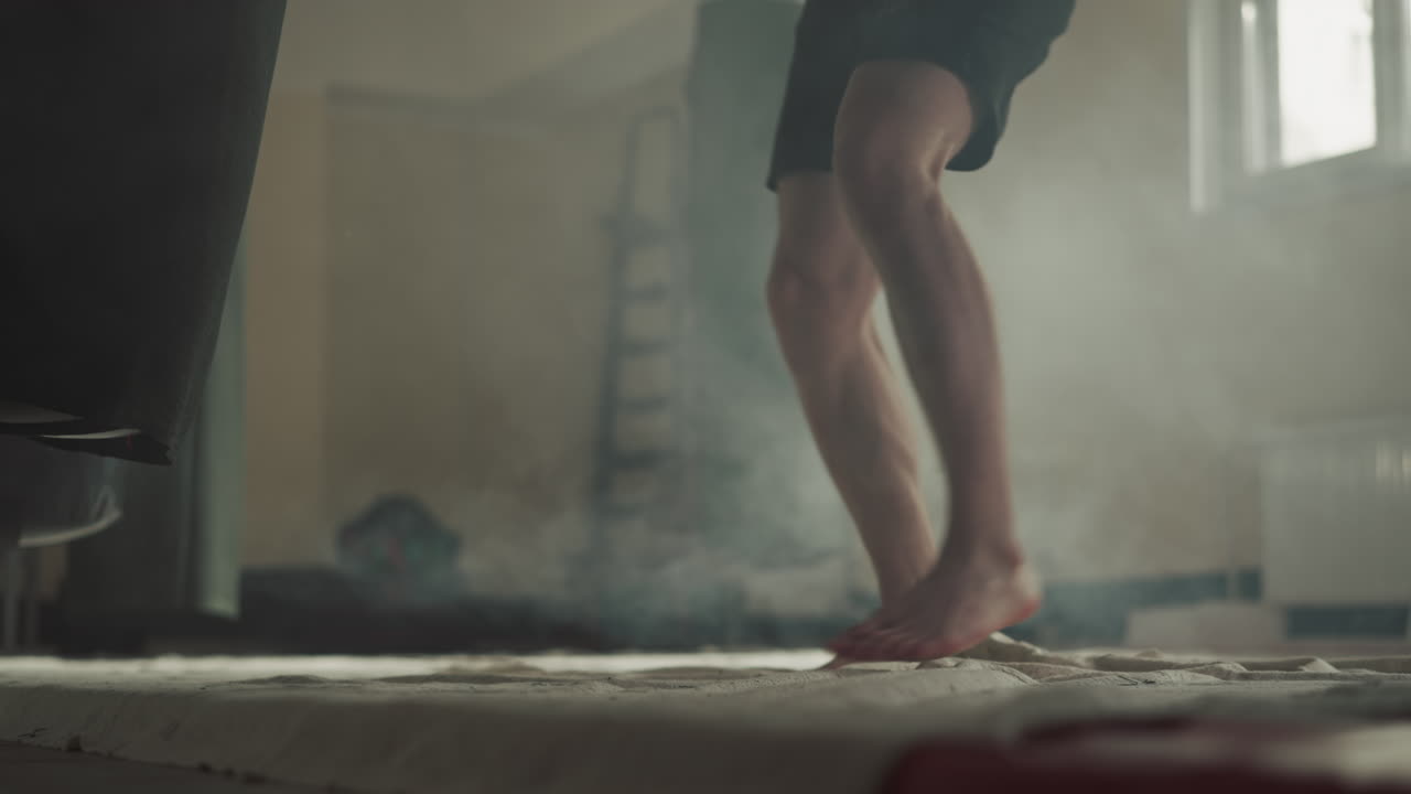 Barefoot man hits punching bag by knees in gym closeup. Professional sportsman trains leg kicking with heavy equipment in sports club slow motion