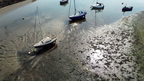 aerial birdseye above boats in shimmering sunny patterned sand beach at low tide marina pull back tilt up to horizon
