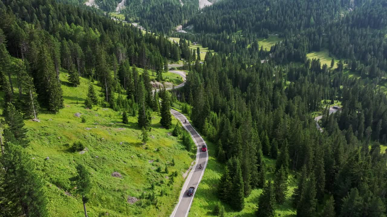 Curved mountain road in lush green Alps, drone tracks moving traffic below