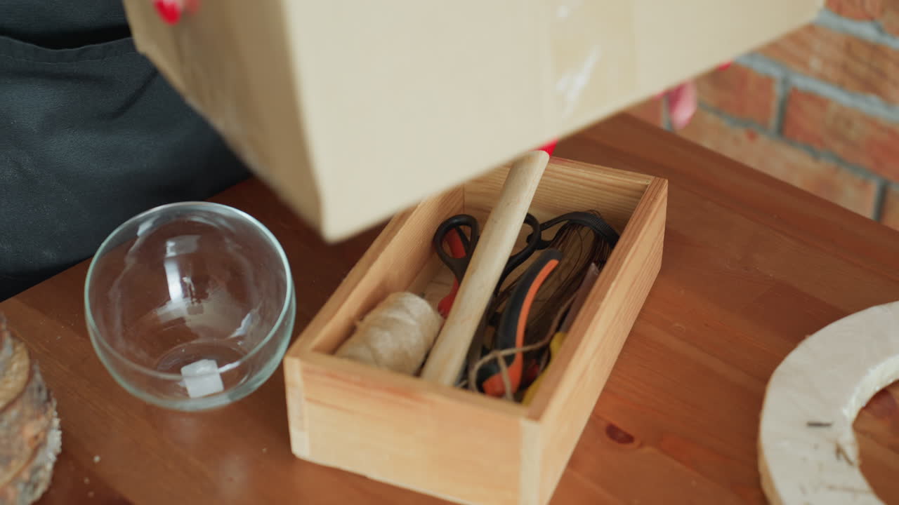 Florist with blonde hair wearing apron working in workshop, close up portrait with thoughtful focused expression, preparing handmade arrangement while standing near brick wall background