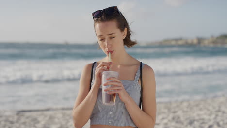 portrait-of-beautiful-young-woman-sipping-juice-on-sunny-beach-enjoying-warm-summer-vacation-day-at-fresh-ocean-seaside-background