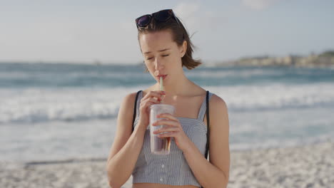 retrato de una hermosa mujer joven bebiendo jugo en una playa soleada disfrutando de un cálido día de vacaciones de verano en el fondo fresco de la costa del océano