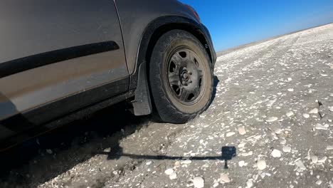 Low-view-of-SUV-racing-across-beach-and-sandy-road-with-blue-sky