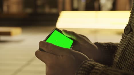 back view close up man hands holding chromakey green screen smartphone watching content, play game, swiping scrolling on sofa at home. gadgets people concept.