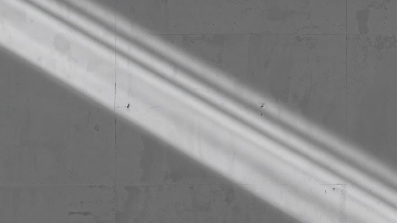 Banda de luz triple diagonal deslizante desplazándose por la pared gris de una habitación, procedente de las persianas
