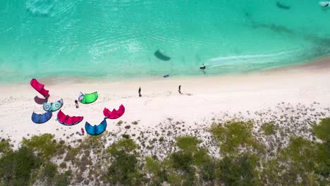 Aerial-top-down-man-kitesurf-along-shore-beach,-kite-camp-on-crasqui-tropical-island