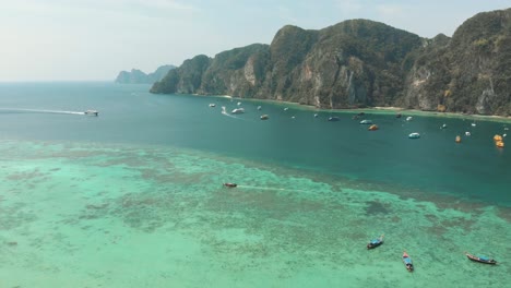 busy harbour in tonsai bay with long-tail boats and small yachts moored in ko phi phi don island, thailand - aerial descend overview shot