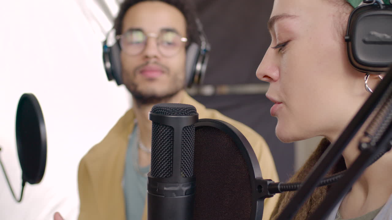 vista de cerca de una mujer que usa audífonos sentada en una mesa con micrófonos mientras graba un podcast con un hombre