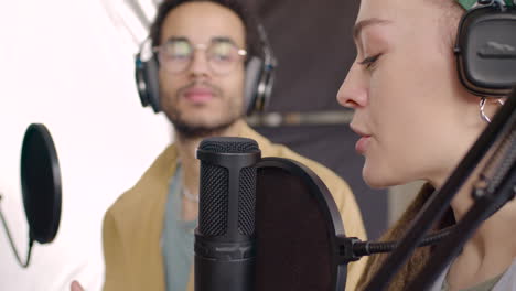 vue rapprochée d'une femme portant des écouteurs assise à une table avec des microphones tout en enregistrant un podcast avec un homme