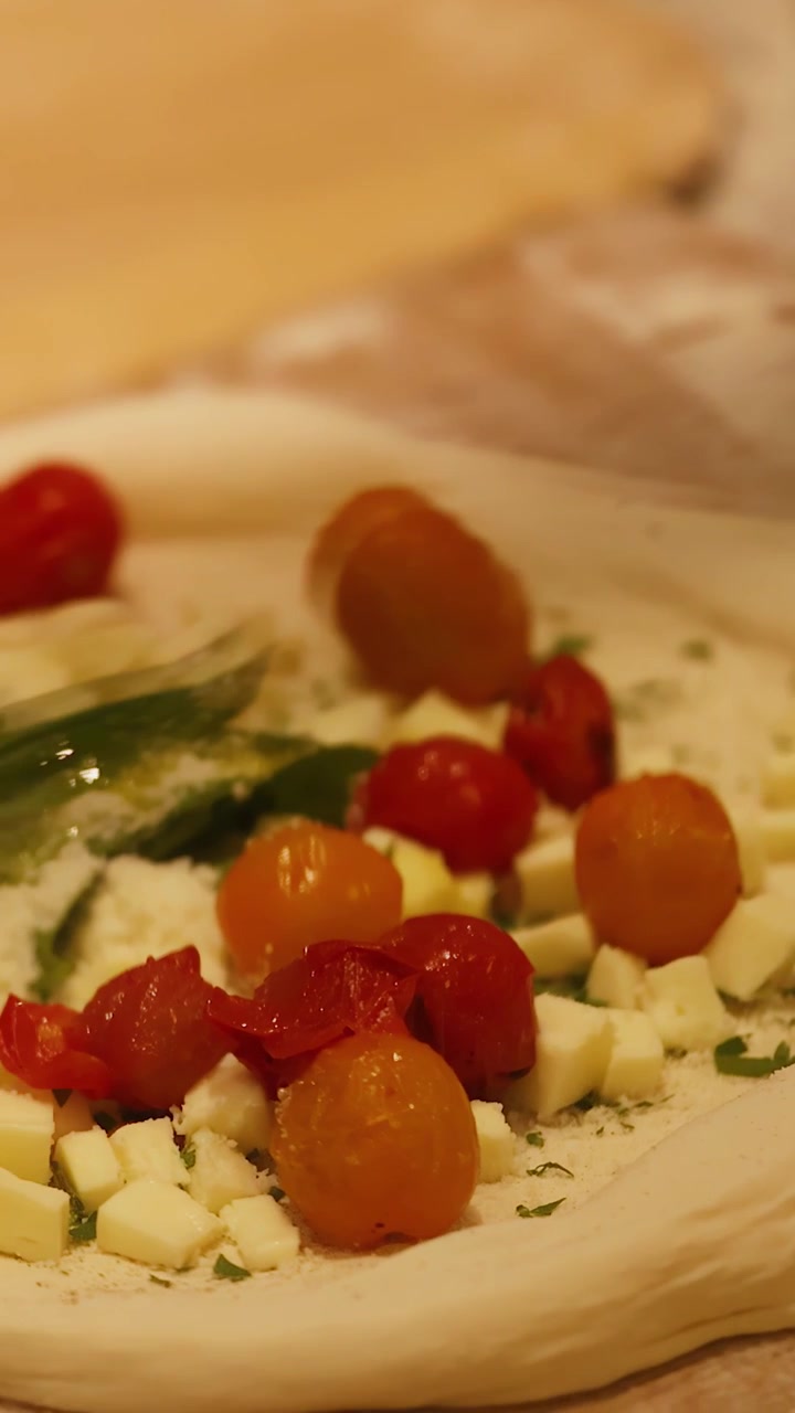 Primo piano di impasto crudo per pizza guarnito con pomodorini, formaggio e basilico su superficie di legno