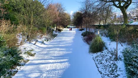 an adult and a child walking down a snowy path in an urban park