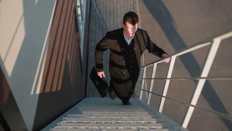 businessman climbing staircase, switching briefcase from left hand to right hand, sunlight reflecting off face, with iron railing on the stair case and casted shadow on the ground