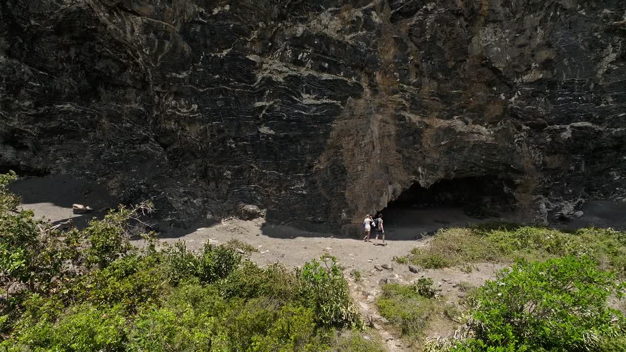 una pareja caminando bajo un acantilado rocoso a lo largo de la playa fronton, las galeras en la república dominicana