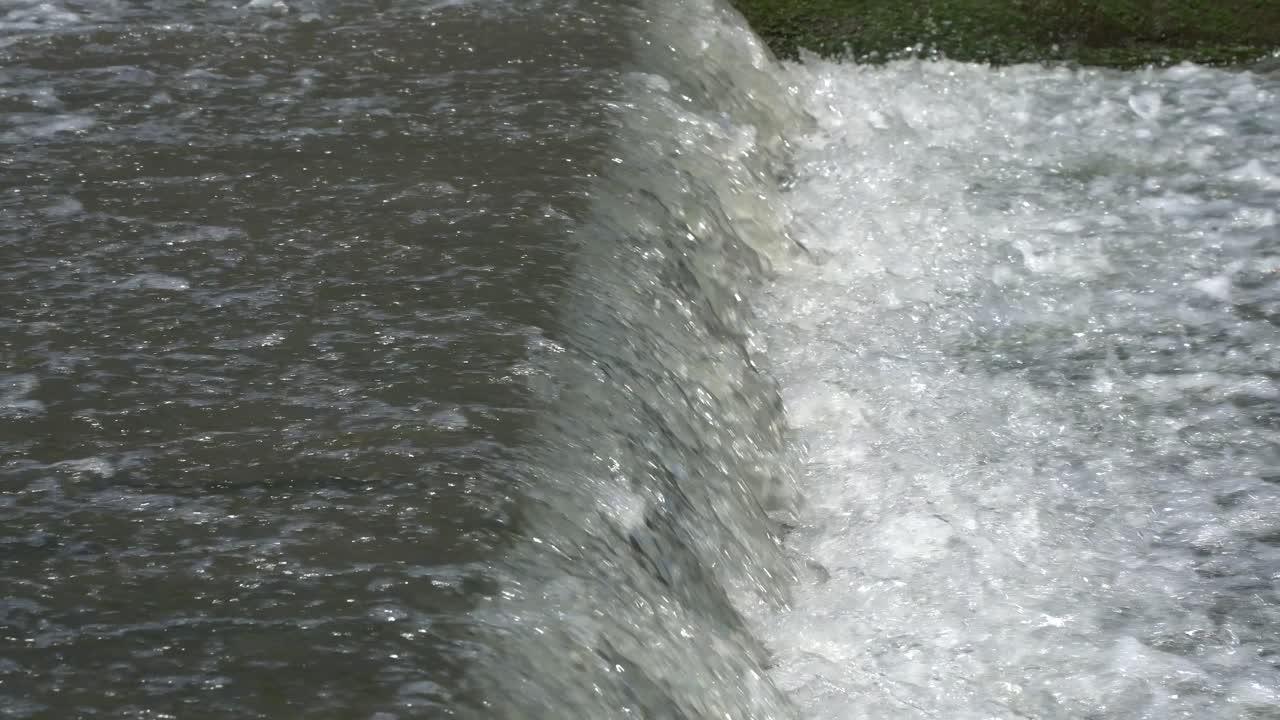 Splashing water flows over a small artificial cascade waterfall closeup side view