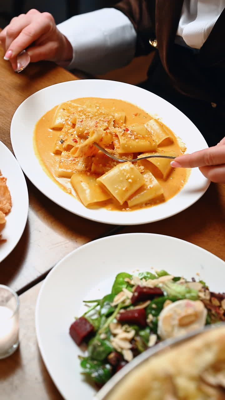 Diners enjoy a meal featuring pasta, salad, and appetizers at a restaurant. Diners share a table, enjoying pasta in sauce, fresh salad, and fried appetizers during dinner service