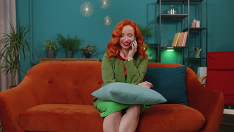 mujer de cabello rojo disfrutando de una llamada de teléfono inteligente hablando, conversación por teléfono móvil con amigos en casa