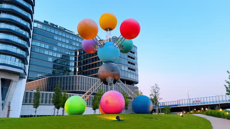 colorful sculpture in modern urban park. large, vibrant spheres adorn a structure in a contemporary park, surrounded by buildings during twilight
