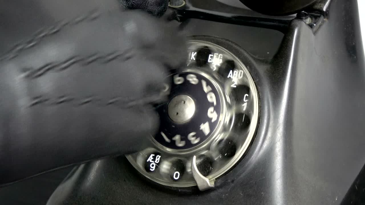 검은 장갑을 입은 스터 손이 오래된 전화 다이얼을 다이얼합니다.