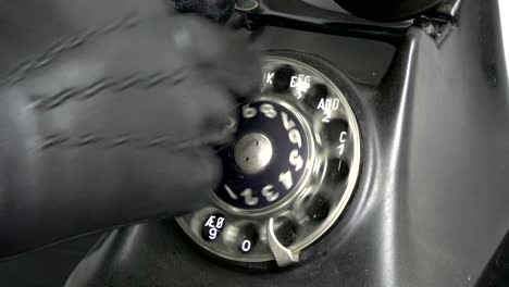 mano de gángster con guante negro marcando viejo dial de teléfono