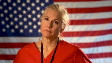 Female-nurse-walking-from-out-of-focus-US-flag-to-a-medium-tight-portrait-looking-very-sad,-worried-and-concerned