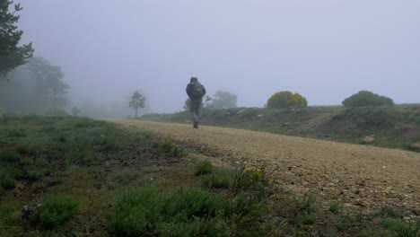 a man going up a trail wiyh a backpack in a foggy an cold day in te muntain