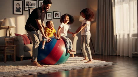 family fun: father and kids playing together on an exercise ball indoors