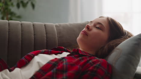 Tired-young-woman-in-checkered-shirt-falls-down-onto-sofa