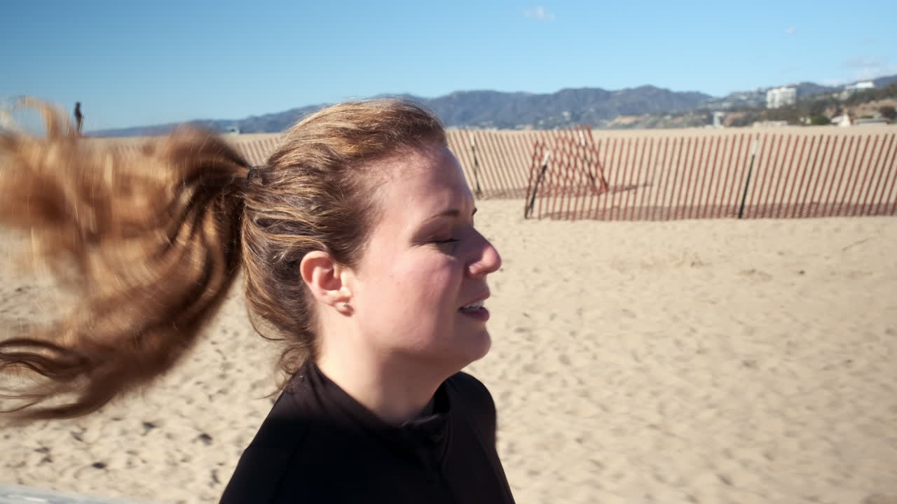 Donna fitness concentrata che fa jogging in una giornata di sole intenso sulla spiaggia di Santa Monica, California.