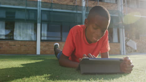 lying on grass, boy using tablet for schoolwork outside school building