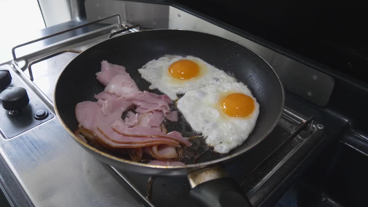 Bacon and eggs frying an a pan on a gas cooker in a campervan or motorhome