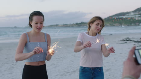 group of friends lighting sparklers celebrating on beach posing for photo dancing happy