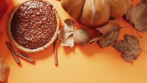 video of autumn leaves, pumpkin, spices and pie on orange background