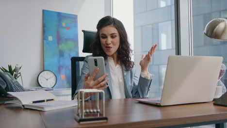 una chica segura con una pantalla de teléfono inteligente se siente sorprendida en la oficina de cerca.