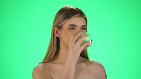 disparo de cámara lenta de una mujer joven con labios hermosos llenos bebiendo un vaso de agua para saciar su sed contra un fondo verde