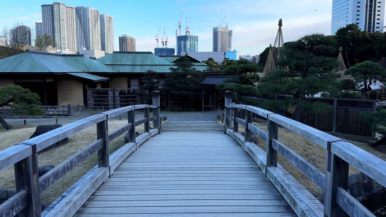 A peaceful wooden bridge in Hama Rikyu Gardens with a cityscape in the background