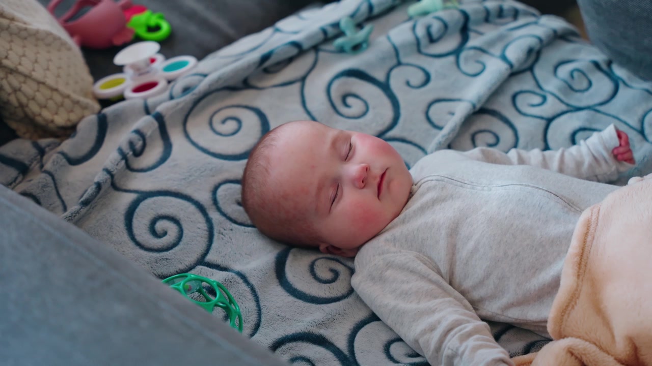 Inquadratura statica che guarda dall'alto una bambina che dorme, riposando pacificamente su un divano circondata da giocattoli all'interno di una casa familiare