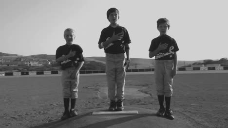 fotografía en blanco y negro de jóvenes jugadores de béisbol que cubren sus corazones con sus sombreros