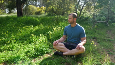 a man sitting in a grassy forest meadow in nature on a beautiful sunny day thinking about his life and meditating to increase happiness