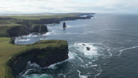 kilkee cliffs in ireland with lush greenery and ocean waves crashing against rocks