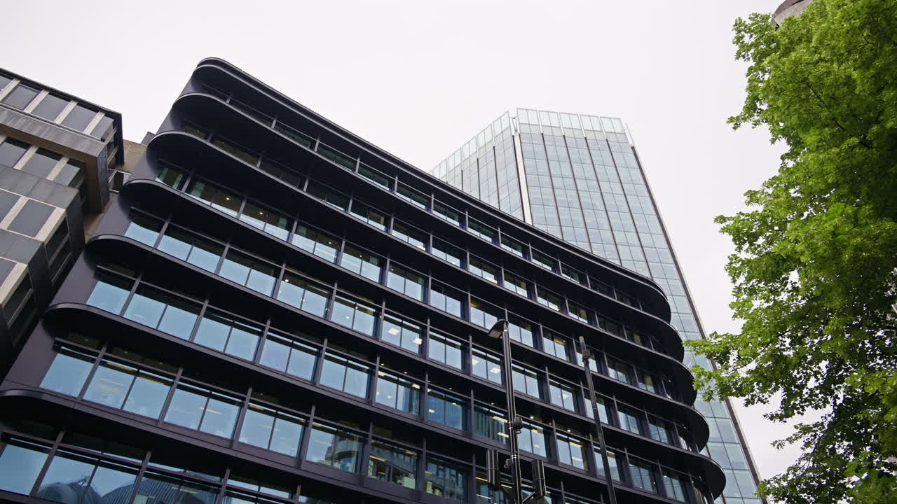 View of a sleek modern office building with large glass windows reflecting the city, surrounded by trees in London, England